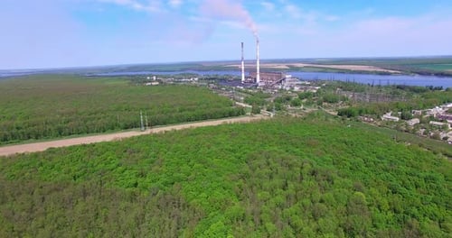 Flying over abundant green forest closer to an industrial zone.