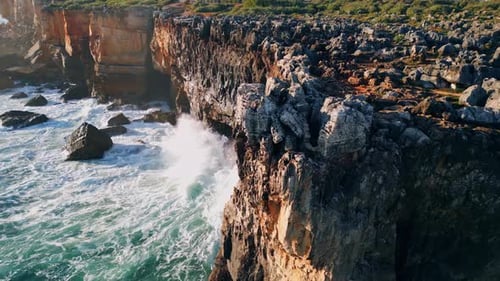 Drone view of powerful ocean waves crashing on rough volcanic cliffs at sunny day