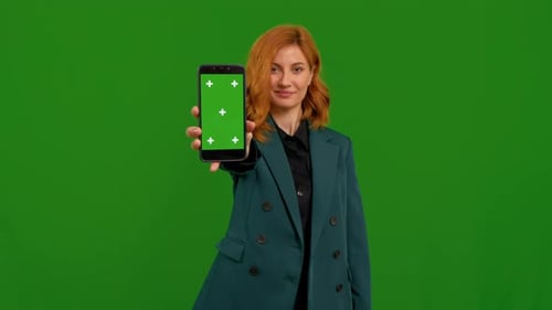 Portrait of business woman showing mock up smartphone to camera with smile over green screen backgro
