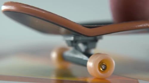 A hyper close-up detailed shot of a mini skateboard, tiny white wheels, riding fingerboard from righ