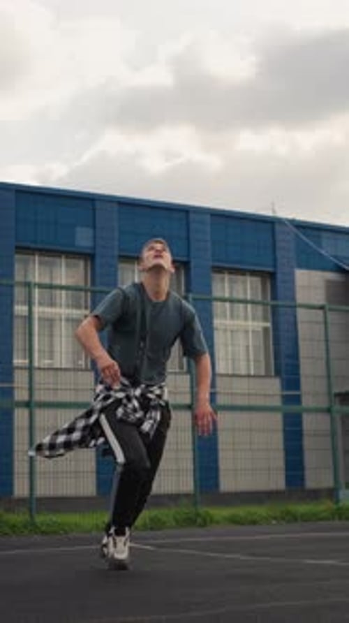 Athlete Throws Up Volleyball and Hits It on Basketball Court with Blue Building in Background