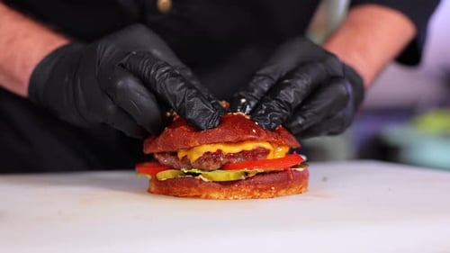 The Cook in the Kitchen Prepares a Cheeseburger and Puts a Cutlet with Melted Cheese