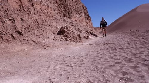 Male hiker walking along desert sand cliff in Chile approaches camera