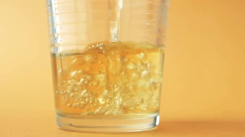 Apple Juice Pouring into Glass on Orange Surface