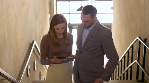 Smiling businesswoman and businessman use tablet technology in modern office