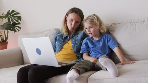 Happy mother and kid son watching videos in computer laptop inside living room at home - Family love