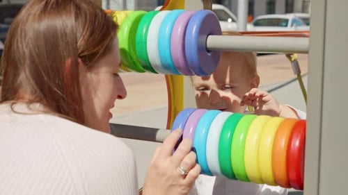 Young mother teaching her baby son using colorful abacus on playground