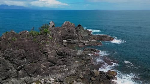 the drone shot glides along the coastline, offering a sweeping view of the small rocky mountains ris