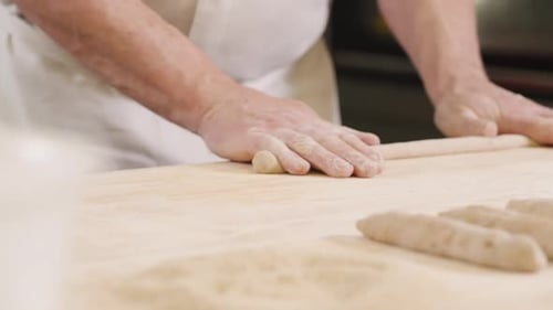 European senior baker rolling raw dough on wooden desk, bakery chef rolling out dough for bread roll