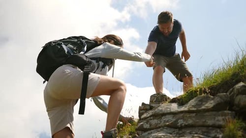 A carefree happy tourists couple is helping to each other to climb on a peak while hiking in the m