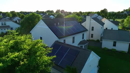 Aerial rotation around solar panels on rooftop of residential home. Green foliage and sunset in a be