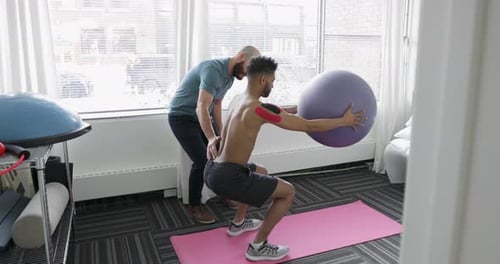 Man squats with exercise ball and instructor