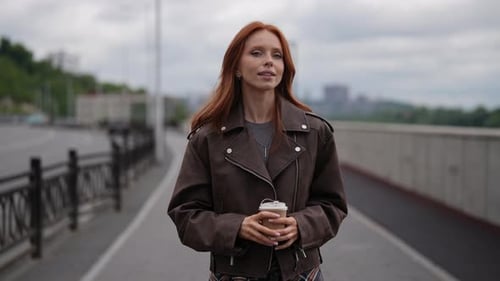 Stylish Redhead Young Woman Walking on City Bridge with Coffee Exuding Confidence and Happiness in