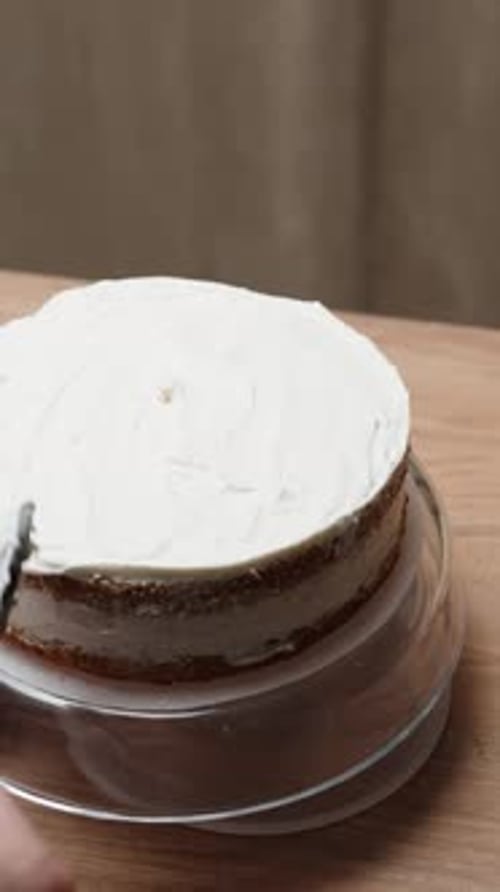 View from behind the woman who is smoothing out the cream on the cake in slow motion Vertical video.
