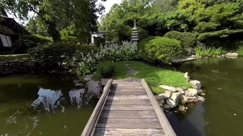 Steadicam shot crosses foot bridge of pond up to stone pagoda, flowers and Japanese lantern.