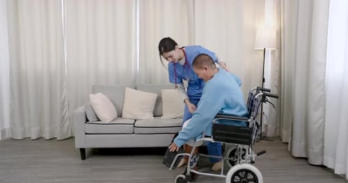Caregiver Helping Senior Man Into Wheelchair Indoors