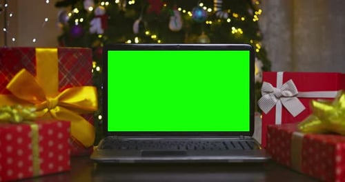 Laptop with Green Screen Surrounded By Gifts on Background of Christmas Tree