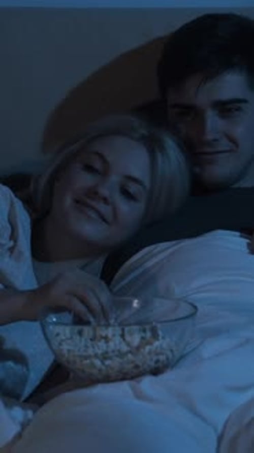 Young Couple Relaxing in Bed with Popcorn at Night