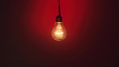 Incandescent Lamp Glows and Flickers on Dark Red Background Place for Text