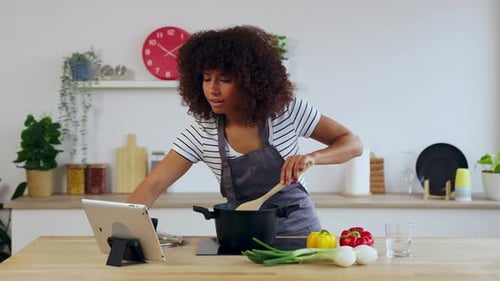 Mujer joven cocinando y siguiendo la receta en una tableta digital en la cocina