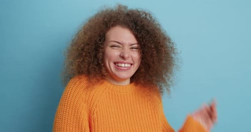 Smiling woman in orange sweater against blue background