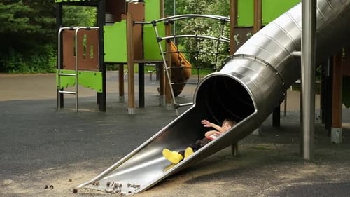 Metal Tube Slide on the Playground Boy is Going Down and Having Joy and Fun