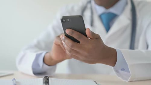 Close Up of African Doctor Browsing Internet on Smartphone
