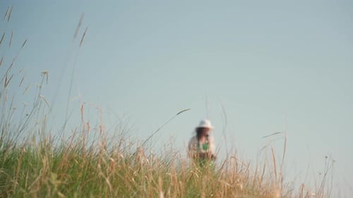 Close Up of Tall Grass with Blurred Woman Taking Photo in Background