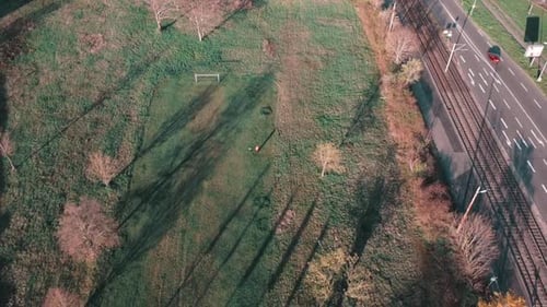 Drone view onto a football field and a street white cars with shadows from the setting sun in centra