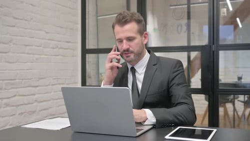 Man in Suit Using Laptop and Phone in Office