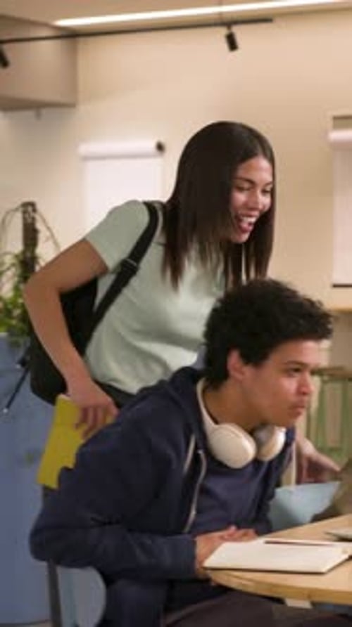 Vertical video: Approaching woman raising hand, seated man gesturing at laptop, studying on campus