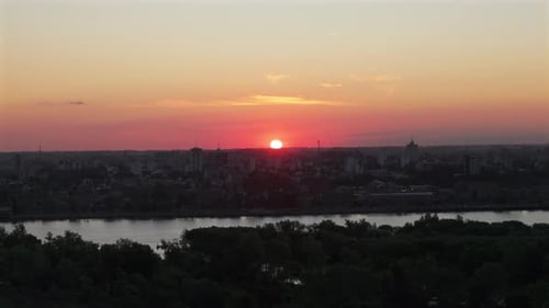 Sonnenuntergang über der Skyline der Stadt mit einem Fluss, der warme Orange-Rosatöne reflektiert, Luftaufnahme