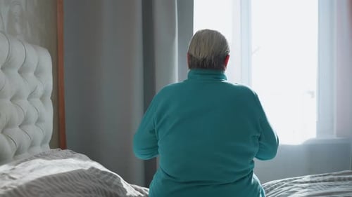 Woman Sits Quietly on Bed in Sunlit Bedroom