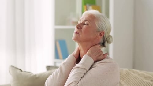 Senior Woman Massaging Her Neck in Indoor Setting