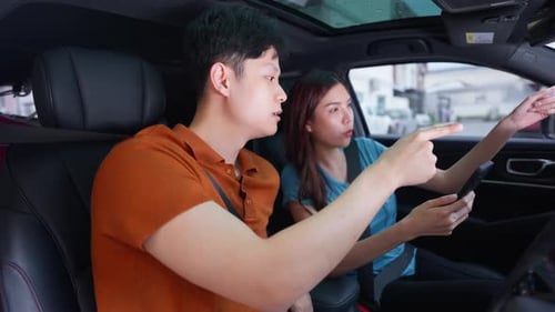 Asian couple looking at map application on a smartphone before driving.