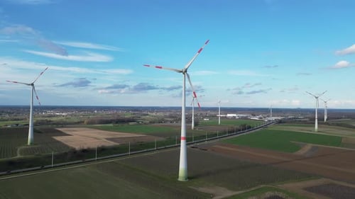 Descending aerial of windmill farm next to highway in rural landscape
