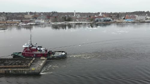 Close up aerial footage of flying over small tugboat pulling barge, forward flight over to town of B