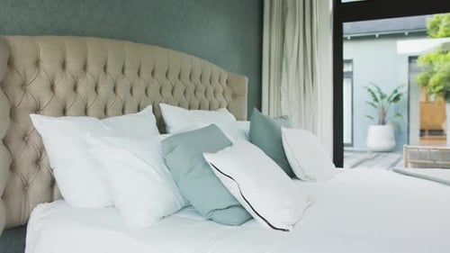 General view of bed with white sheets, big window and view to garden in bedroom, slow motion