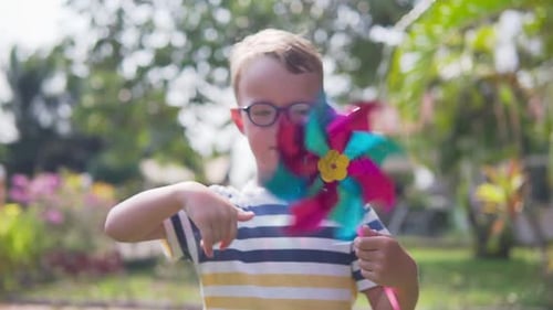 Boy in glasses is playing with pinwheel in a garden