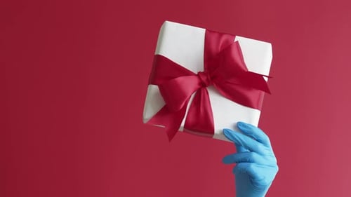 Gloved Hand Holds Present Box with Red Bow