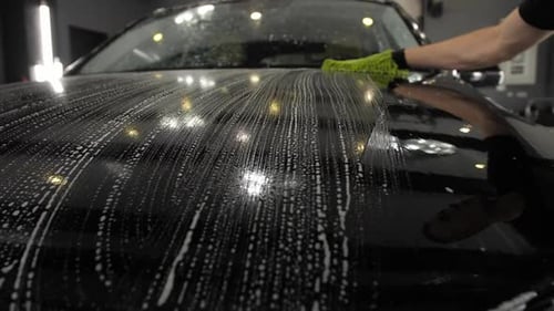A Worker with a Green Sponge Cleaning Foam Hood and Car Headlight
