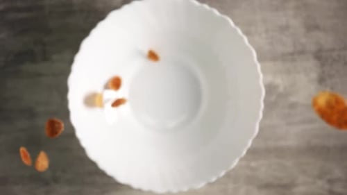 Gelbe Cornflakes zum Frühstück fallen in großen Mengen in Zeitlupe von oben auf den Teller