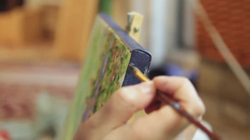 Weibliche Hand, die einen Pinsel hält und den Rand der Leinwand bemalt, um das Kunstwerk in einer Studioumgebung fertigzustellen