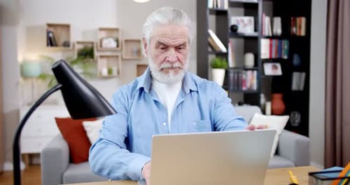 Senior Man Types on Laptop Computer at Home