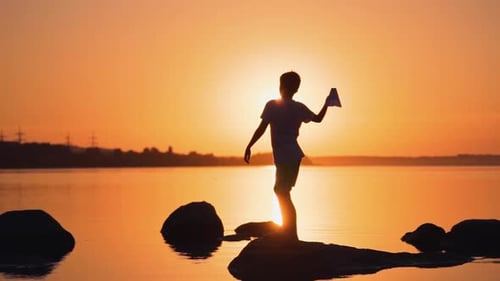Child Silhouette Throws Paper Airplane at Sunset