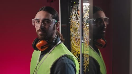 Man with Safety Gear Stands by Server Cabinet