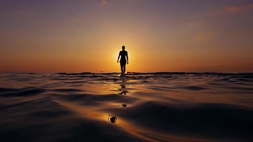 Wide Angle View Of Lone Person Walking Through Sea Toward Sunset With Centered Silhouette And Warm L