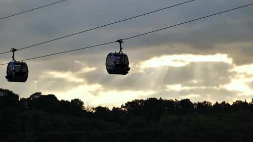 Cable Cars Silhouetted at Sunset Above Dense Forest