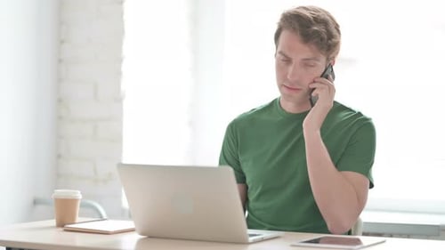 Man Talking on Phone at Laptop Workstation