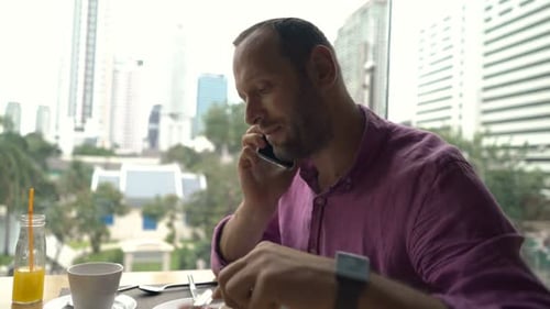 Young Man Talking on Cellphone During Meal in Cafe 30s